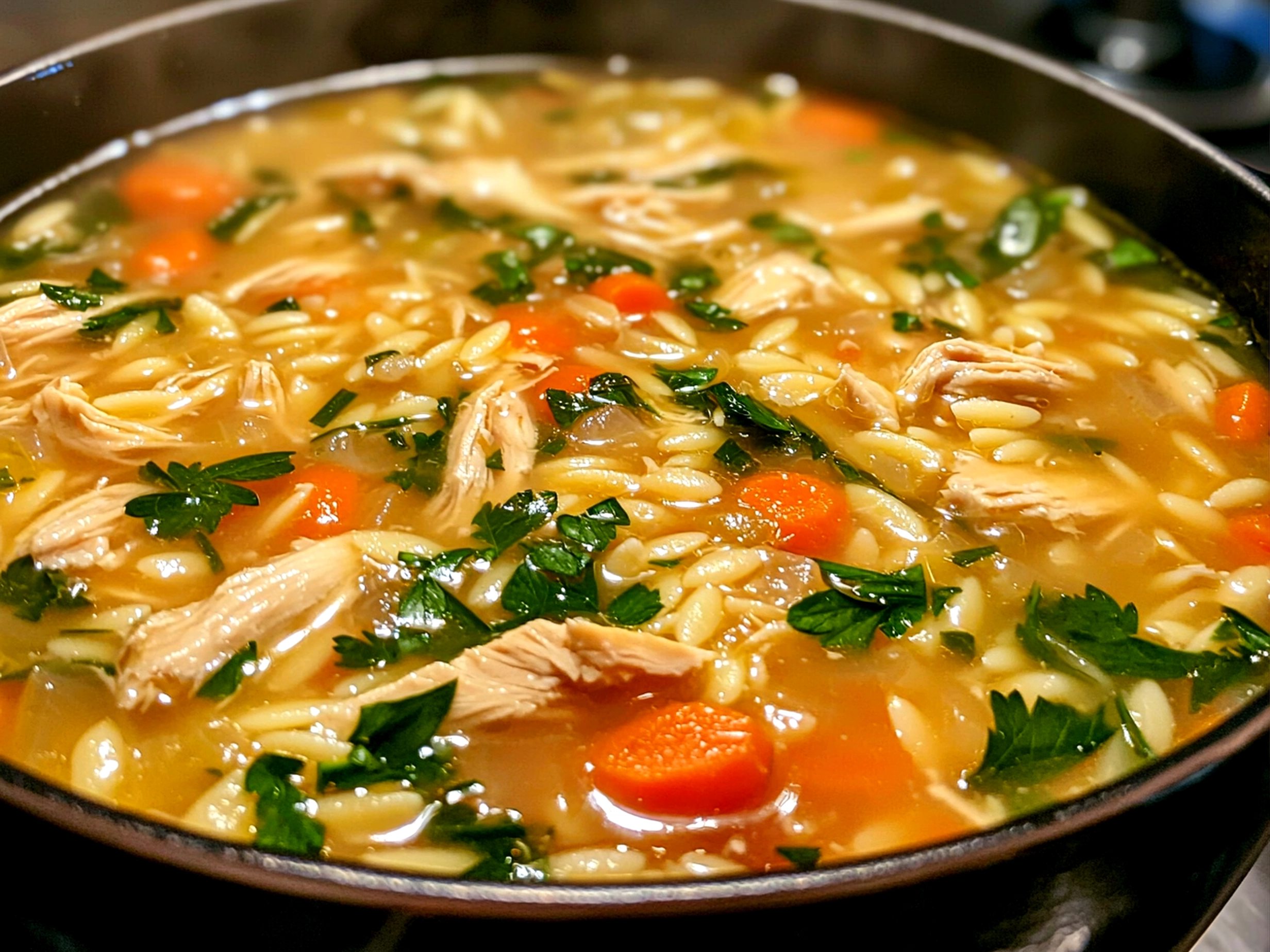 A bowl of Spring Chicken Soup with Orzo garnished with fresh herbs